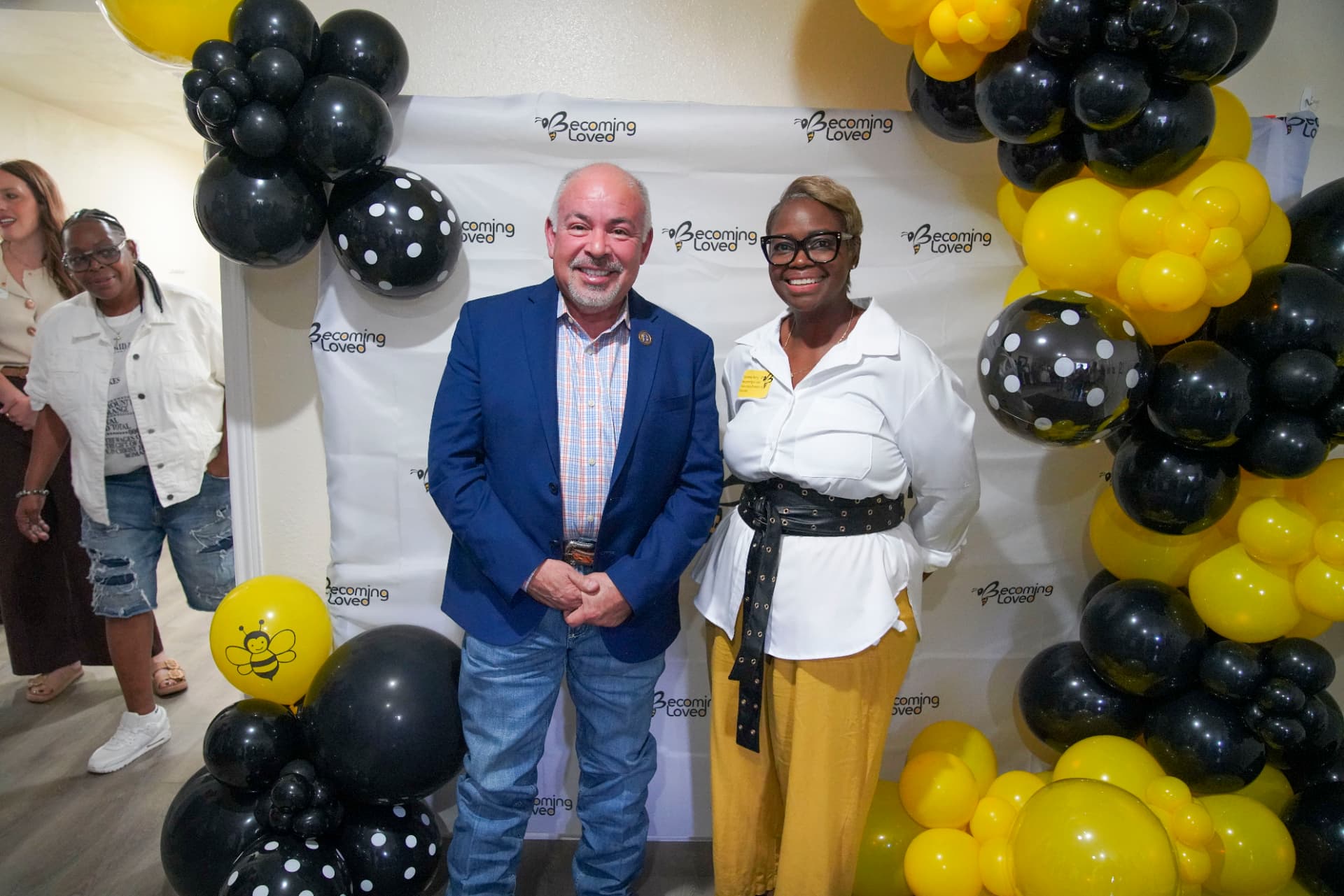 Two attendees smiling in front of the Becoming Loved backdrop